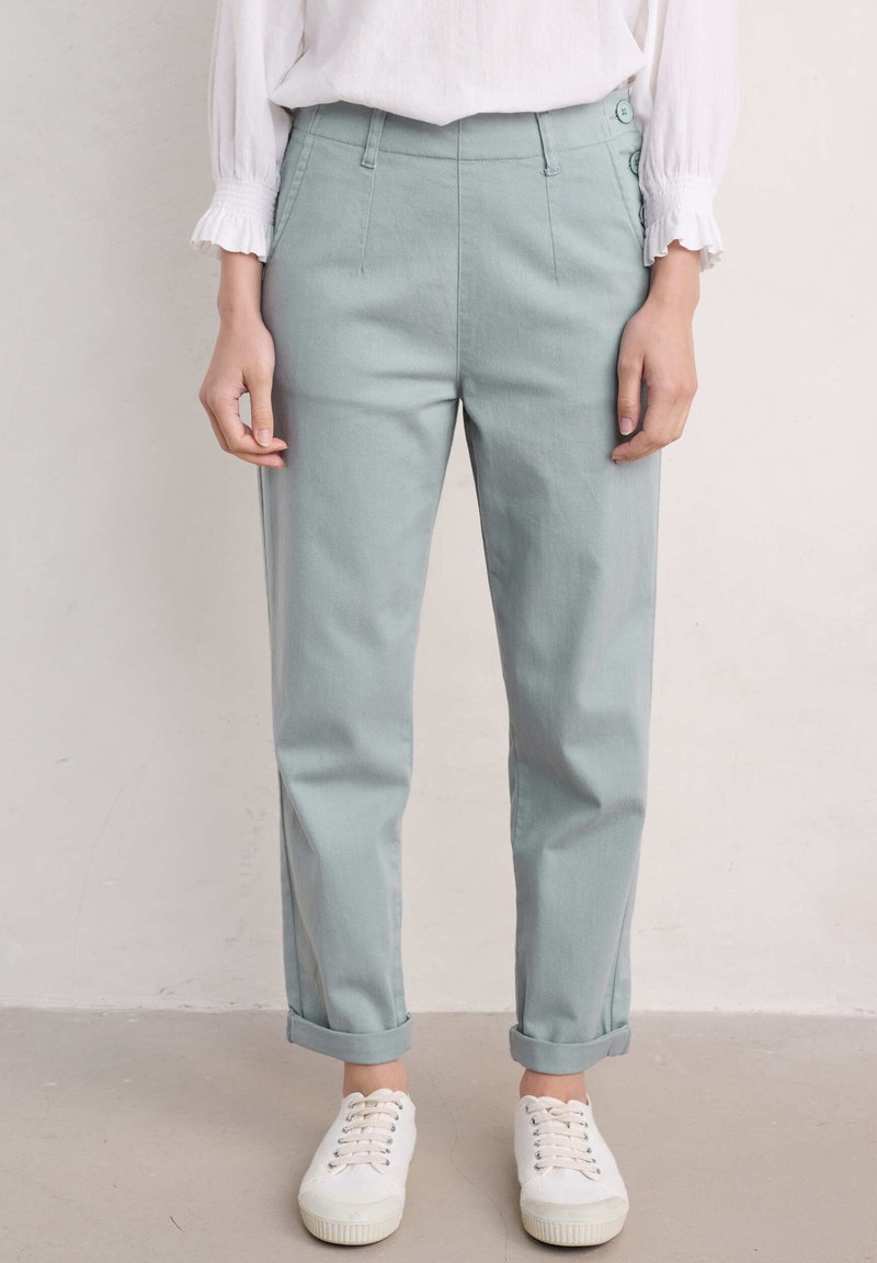 Pantalons taille haute vert clair en mélange de coton, avec des ourlets roulés, des plis à l'avant et deux boutons latéraux à la taille.