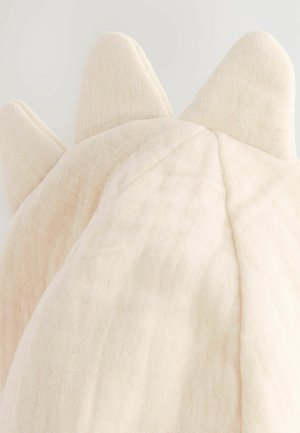 Das Kissen hat einen weichen, strukturierten cremefarbenen Stoff mit drei spitzen Erhebungen an einer Kante, die einem stilisierten Wesen oder einer Blume ähneln.