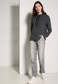 Svart och grå randig huvtröja med dragsko, kombinerad med ljusgrå jeans och vita sneakers för en avslappnad outfit.