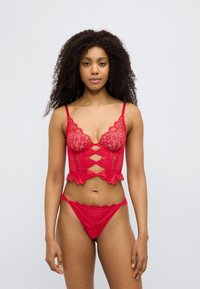 Σετ εσωρούχων από κόκκινη δαντέλα που περιλαμβάνει ένα σουτιέν με κυματιστή άκρη και λεπτομέρεια με άνοιγμα, συνδυασμένο με σλιπ από δαντέλα που ταιριάζει. Ομαλή υφή.