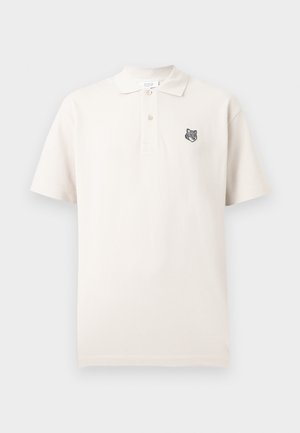 Polo crème à manches courtes avec deux boutons et une petite tête de loup brodée sur le côté gauche de la poitrine.