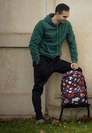 Mochila negra y con estampado de personajes de dibujos animados; correas de tela, doble cremallera y un bolsillo delantero. Sudadera verde y pantalones de chándal negros.