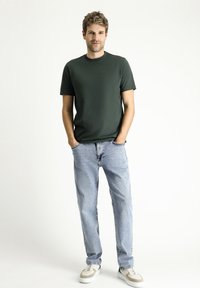 Donkergroen T-shirt met korte mouwen, gecombineerd met lichtblauwe rechte jeans en grijze sneakers, met subtiele stikdetails en een relaxte pasvorm.