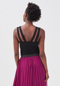 Haut noir sans manches avec double bretelles, associé à une jupe plissée magenta. Texture lisse avec un design ajusté à la taille.