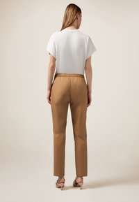 Pantaloni marroni con vita elastica, dal taglio rilassato e gamba affusolata, abbinati a una camicia bianca a maniche corte, visti da dietro.