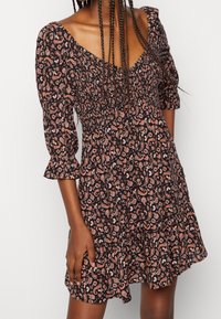 Černé šaty s květinovým paisley vzorem v růžové a bílé barvě, s nařaseným živůtkem, volnými rukávy a volánkovým lemem.