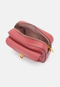 Borsa a tracolla rossa in pelle con forma arrotondata, accessori in oro e chiusura con zip superiore. L'interno presenta una fodera liscia e una piccola tasca.