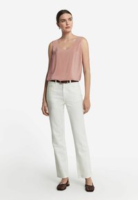 Ljusrosa satin utan ärmar, vita raka jeans, mörka vävda slip-on skor, med ett brunt bälte synligt vid midjan.