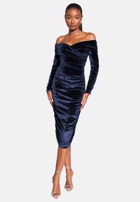 Dziļi zila samta kleita ar atklātiem pleciem, garām piedurknēm, ru�čotu dizainu, vidēju garumu un gludu tekstūru. Saskaņota ar caurspīdīgām siksniņām.