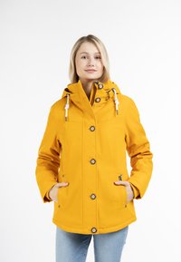 Cazadora amarilla impermeable con capucha; cuenta con cierres de botón, detalles con cordón y bolsillos laterales; textura suave y diseño moderno.