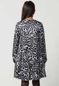 Haljina s printom leoparda koja ima duge rukave, slojevsku suknju i zatvarač na leđima. Izrađena je od glatkog, laganog materijala u crnim i sivoj nijansi.