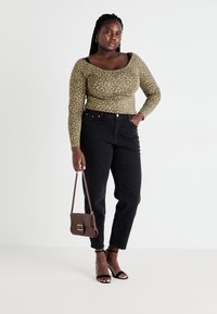 Leopard print long-sleeve top in olive and black, paired with high-waisted black jeans. Model holds a small brown shoulder bag, wearing black heels.