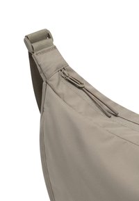 Bežová textilná taška s hladkým povrchom, vybavená zipsovou kapsou a nastaviteľným popruhom pre bezpečné nosenie.