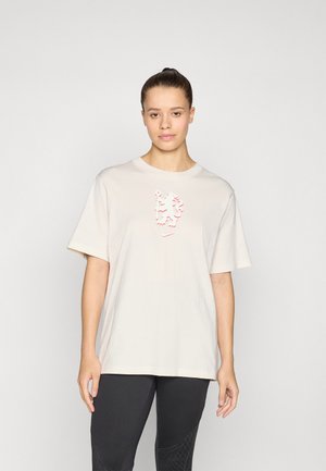 Beige bomull t-skjorte med korte ermer, med et hevet rødt grafisk design på brystet. Kombinert med mørke leggins.