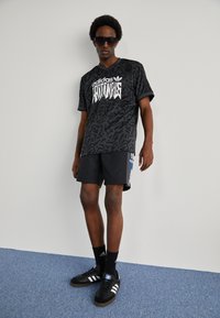 Black Adidas shirt with contrasting graphic design, paired with black shorts. Black sneakers with white stripes and black socks complete the look.