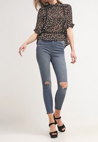 Blouse à motifs noir et blanc à manches courtes, associée à un jean skinny bleu clair à genoux déchirés et des sandales à talons hauts noires.