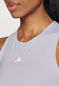 Svetle fialov�ý sportovní tank top s kulatým výstřihem a jemnou texturou. Má viditelné bílé logo blízko límce.