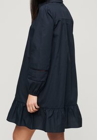 Marineblaues Baumwollkleid mit Kragen, puffartigen Ärmeln und einem welligen Saum. Texturierte Ärmeldetails sorgen für visuelles Interesse.