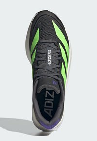 Chaussure de sport noire avec des rayures vertes, tige en maille, col rembourré et accents violets près du talon. Présente le logo "ADIZERO" sur la languette.