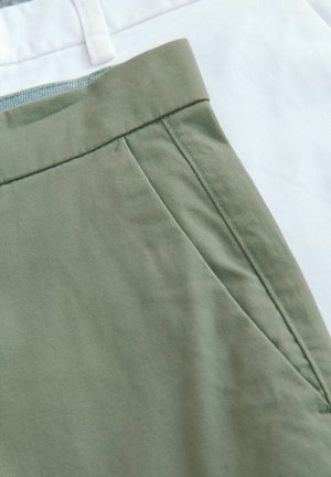 To sæt bukser: et olivengrønt med en glat overflade og sidelomme, og et hvidt med et lysere, skarpt udseende.