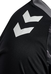 Maillot de sport noir avec une texture lisse, des accents gris et un logo en chevron blanc sur l'épaule. Design sans coutures et ajusté.