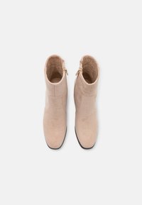 Bottes cheville en daim beige avec une tige lisse, un bout rond et une fermeture éclair latérale. Semelle plate noire avec une légère brillance.