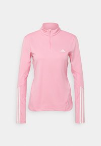 Jasnoróżowa sportowa bluza z wysokim kołnierzem, zamkiem przy szyi, długimi rękawami i trzema pionowymi białymi paskami na każdym rękawie. Białe logo na piersi.