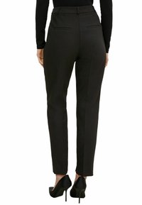 Pantalons noirs ajustés avec une taille haute, dotés de deux poches arrière et d'une coupe slim, assortis de chaussures à talons hauts noires.