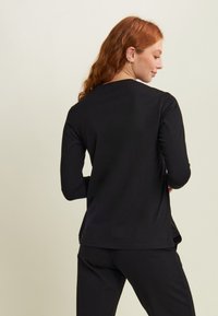 Maglietta nera a maniche lunghe con orlo arrotondato e vestibilità rilassata. Tessuto morbido e fessure laterali per una maggiore libertà di movimento.