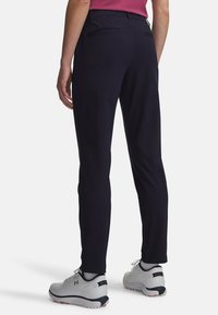 Σκούρο μπλε παντελόνι γκολφ με στενή γραμμή, κατασκευασμένο από ελαφρύ ύφασμα, με πίσω τσέπες και σε συνδυασμό με λευκά παπούτσια γκολφ.