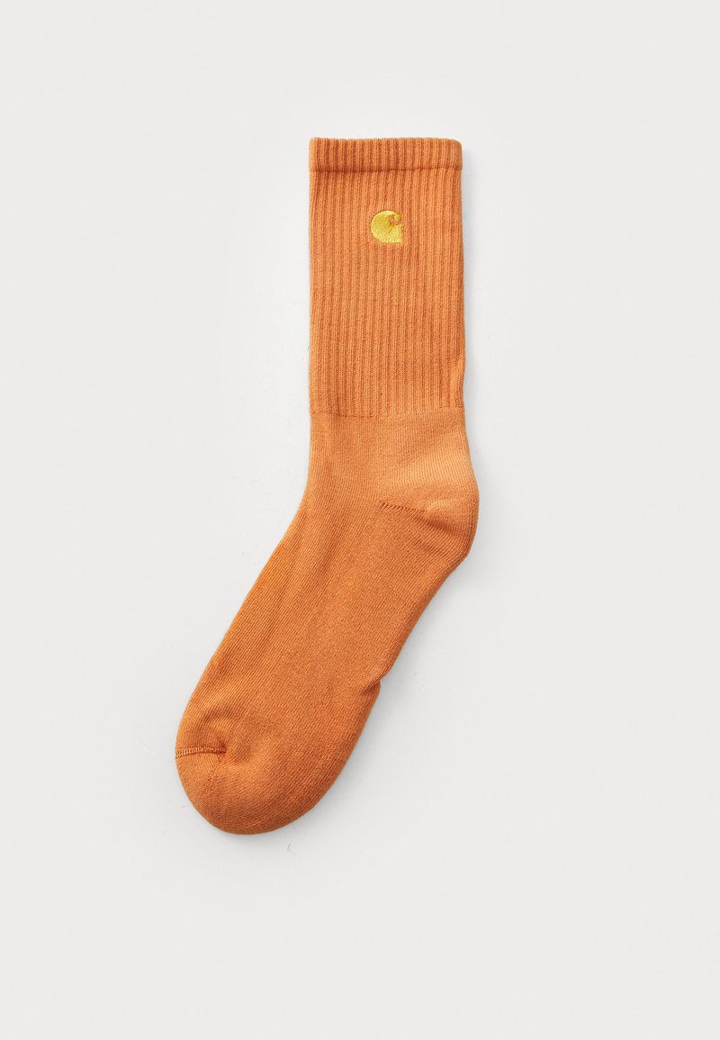 Orange bomuldsstrømpe med ribbet struktur, der har et lille gult logo øverst. Glat finish og standard ankellængde.