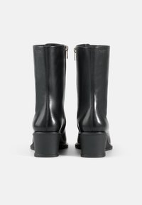 Črne usnjene gležnjarje z sijajno površino, srednjim bloku in zadrgo na hrbtu. Gladka tekstura brez vidnih vzorcev.