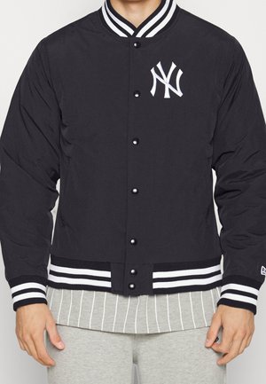 Schwarze Bomberjacke mit weißen Akzenten, die ein New York Yankees-Logo, Druckknöpfe und gestreifte Rippbündchen sowie einen Rippbund am Saum aufweist.