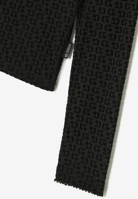 Tissu noir avec un motif en relief présentant des lettres stylisées. Les bords sont ornés d'un délicat motif festonné. Étiquette visible.