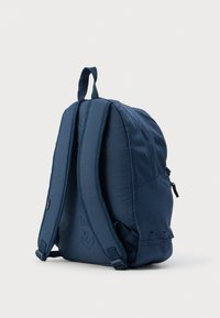 Σκούρο μπλε σακίδιο πλάτης με επενδυμένους ιμάντες, λαβή στο πάνω μέρος, πλαϊνή τσέπη με φερμουάρ και ρυθμιζόμενους ιμάντες με πόρπη σε λευκό φόντο.