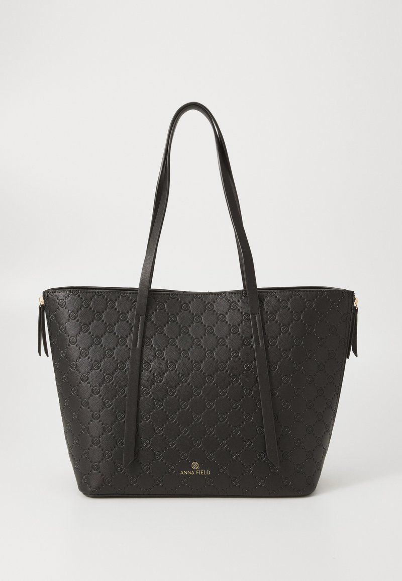 Zwarte tote bag van gestructureerd synthetisch materiaal met een subtiel logo patroon, gladde banden en een gouden merkteken aan de basis.