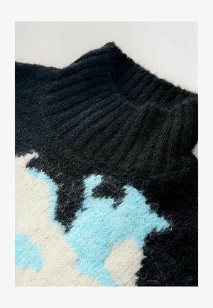 Sort strikket sweater med høj ribbet hals, en tekstureret overflade og et let blå og cremefarvet abstrakt mønster.