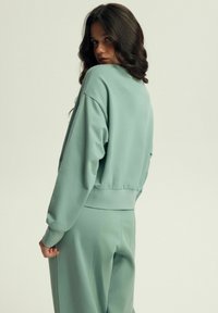 Jasnozielony, krótki sweter z długimi rękawami i ściągaczem, zestawiony z dopasowanymi dresami. Gładka tekstura, luźny krój, minimalistyczny design.