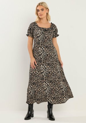 Kvinde iført en leopardmønstret midi-kjole med puffærmer og sorte ankelstøvler, stående mod en ensartet lys baggrund.