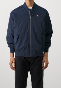 Námořnicky modrá bomber bunda, lehká tkanina, žebrované manžety a lem, přední zip, boční kapsy, malý detail loga na hrudi.