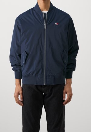 Cazadora bomber azul marino, tejido ligero, puños y bajo acanalados, cierre frontal con cremallera, bolsillos laterales, pequeño detalle de logo en el pecho.