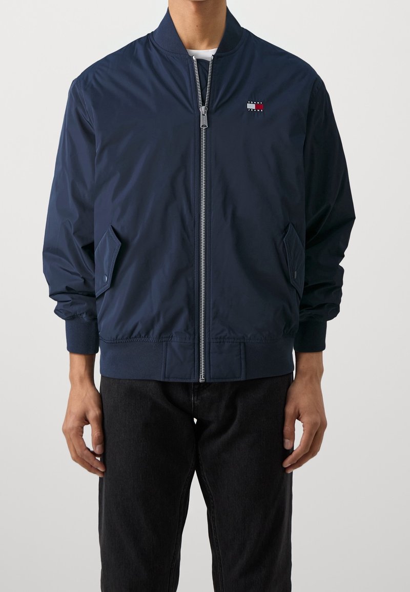 Námořnicky modrá bomber bunda, lehká tkanina, žebrované manžety a lem, přední zip, boční kapsy, malý detail loga na hrudi.