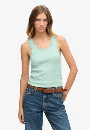 Top de tirantes acanalado en verde menta con detalles de encaje en el escote, combinado con jeans de mezclilla azul de tiro alto y un cinturón de cuero marrón.