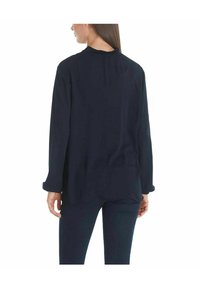 Marineblauwe blouse met lange mouwen, gemaakt van een zachte, gladde stof en een ontspannen pasvorm, met een subtiele plooidetail aan de achterkant en opgerolde manchetten.