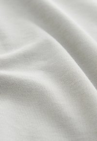 Fehér pamut szövet, finom bordázott textúrával, sima, lágy redőkkel és finom fényvisszaverődéssel. Nincsenek jelentős minták vagy díszítések.