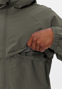 Grüne Jacke mit Kapuze, ausgestattet mit einer sichtbaren Reißverschlusstasche und gefüttertem Innenleben. Elastische Bündchen sorgen für einen sicheren Sitz. Logo auf dem Stoff abgebildet.