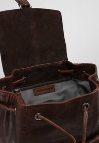 Brun läderbucketväska med en mockaflap, silverfärgad hårdvara och ett fodrat inre med en dragkedjeficka och varumärkesetikett.