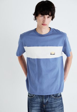 Camiseta de algodón azul claro con una franja blanca horizontal, que presenta un pequeño logo de sol bordado y un corte relajado.