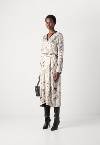 Long-sleeve, white dress with black architectural print, cinched waist with a black belt, paired with knee-high black heeled boots and a small bag.