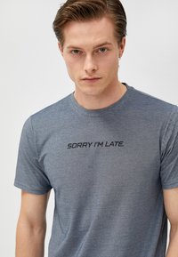 Camiseta de algodón gris con mangas cortas y escote redondo, que presenta el texto "LO SIENTO, LLEGUÉ TARDE" en una fuente negra negrita en el pecho.